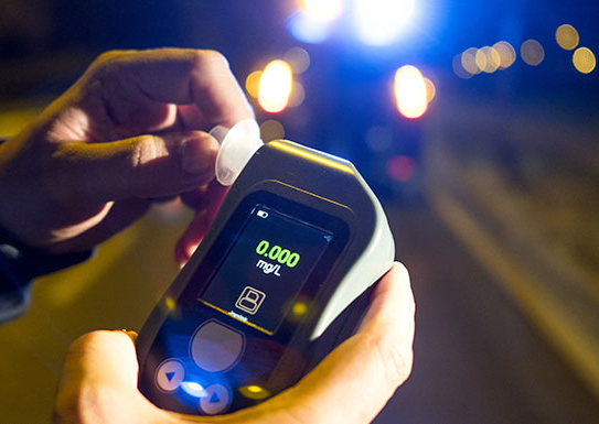 Police officer holding a roadside breathalyzer device during a DUI traffic stop