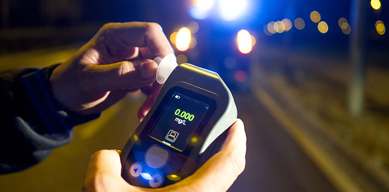 Police officer holding a roadside breathalyzer device during a DUI traffic stop